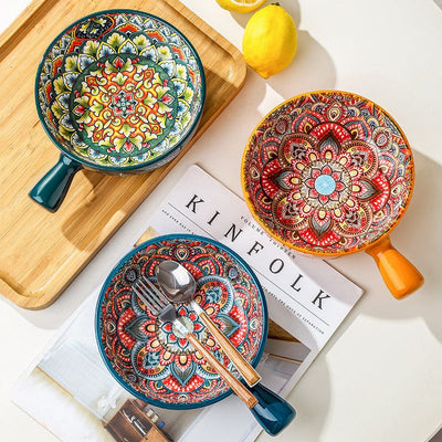 Colorful ceramic glazed salad bowls with flower handle and intricate patterns on wooden tray and magazine with cutlery and lemon nearby
